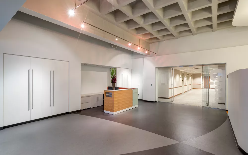 Modern lobby or reception area inside 1818 Market, featuring a sleek wood-accented front desk, geometric ceiling design, minimalist cabinetry, and glass double doors leading to a professional office corridor.